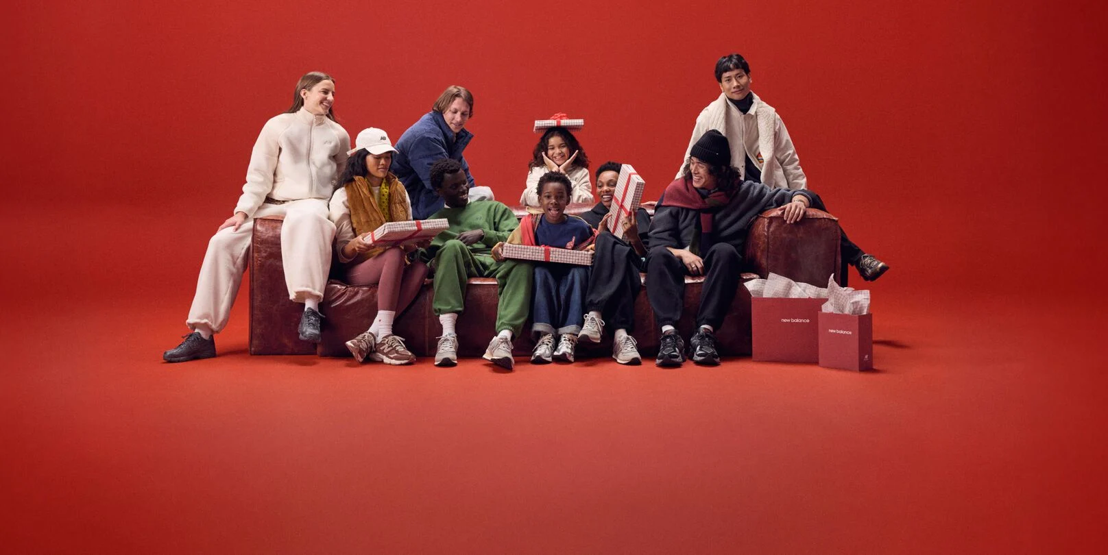 A group of people wearing New Balance sitting on a sofa with a red background.