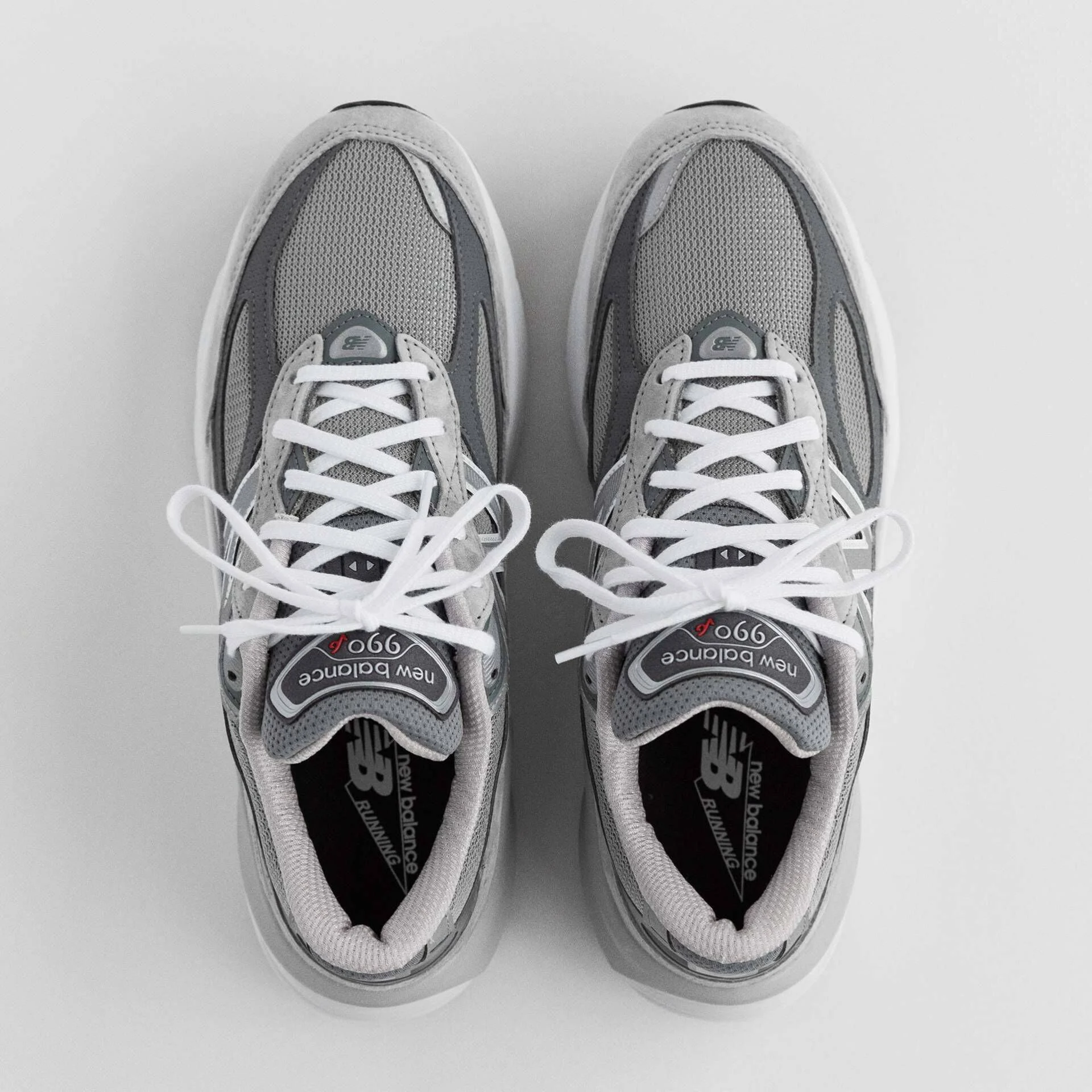 A top-down image of a pair of grey 990v6 sneakers on a grey studio backdrop.