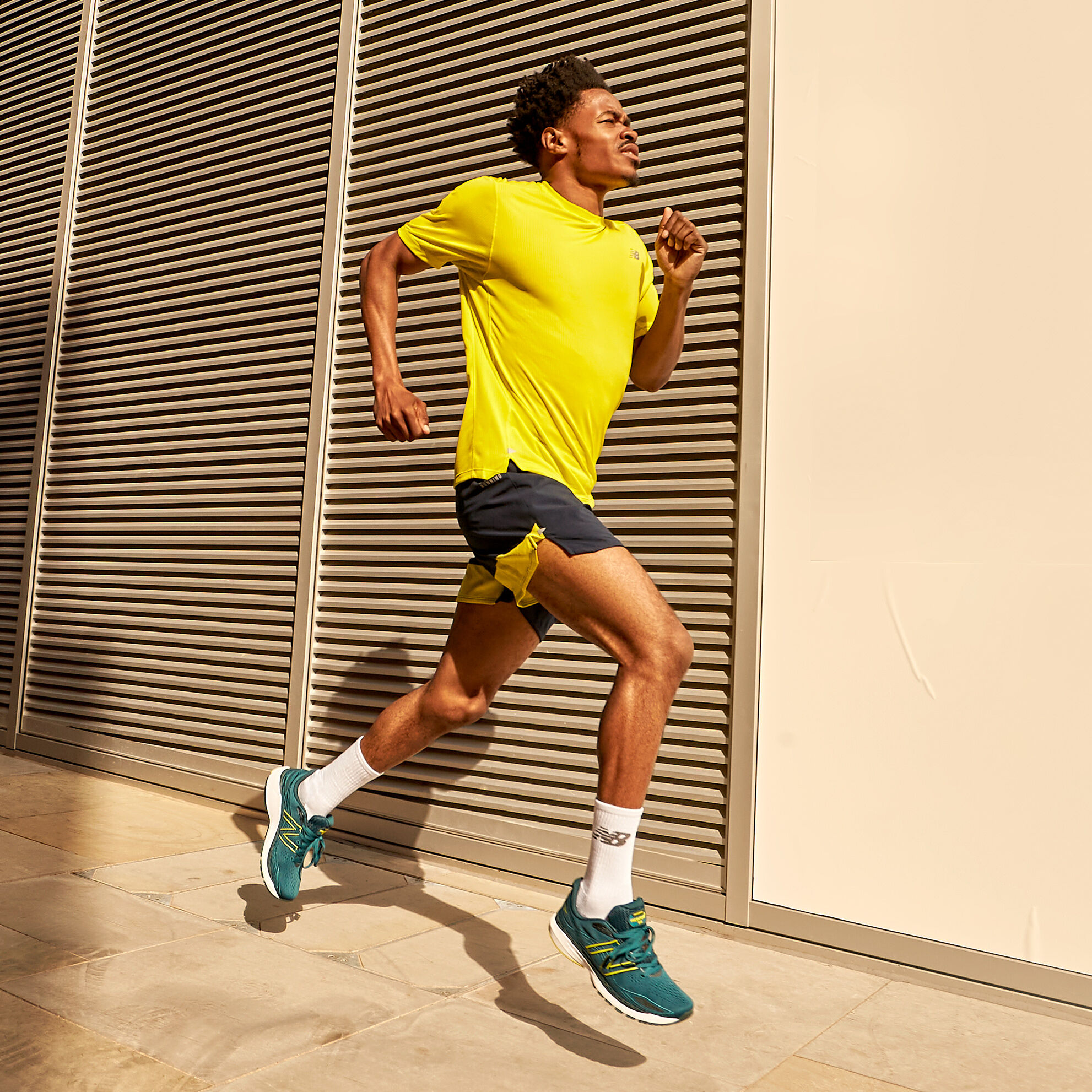 Male runner wearing a yellow shirt, black shorts and the dark green Fresh Foam 860v12 shoes