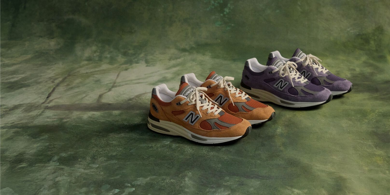 Two pairs of New Balance Made in UK sneakers on a green floor.
