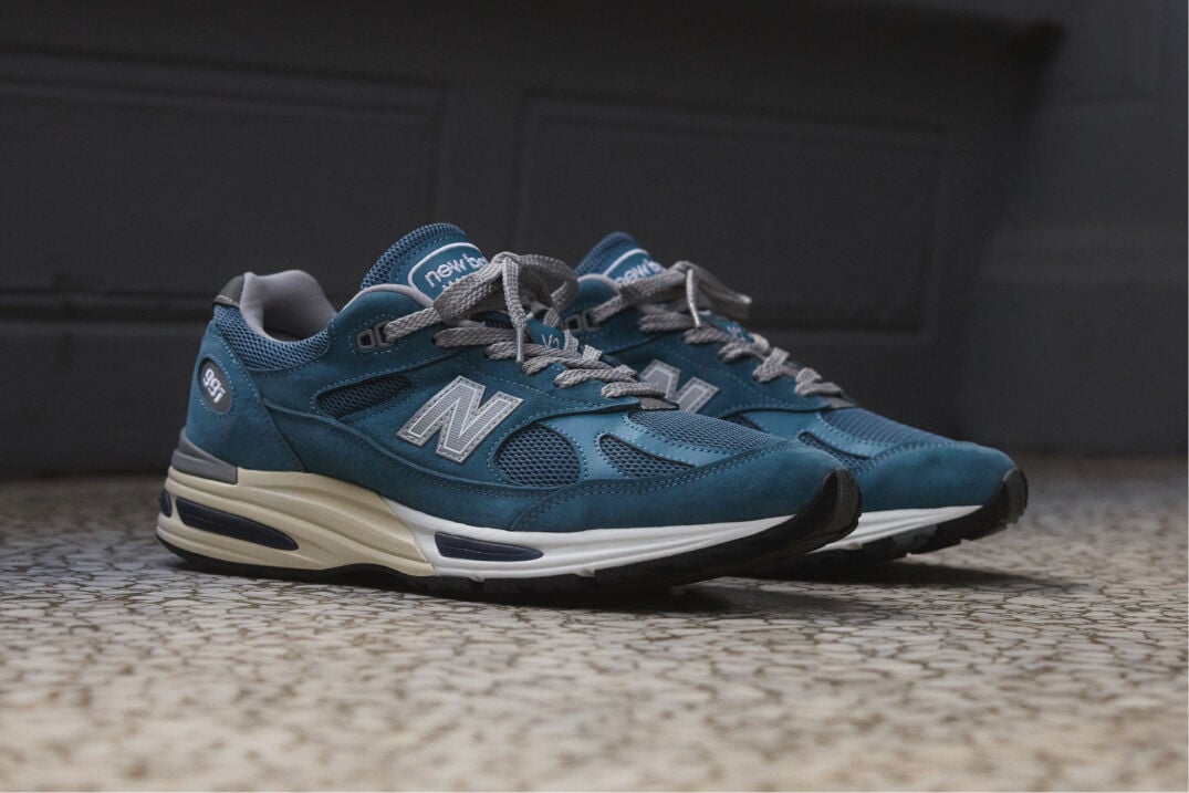 A pair of New Balance Made in UK sneakers sitting on a concrete floor.