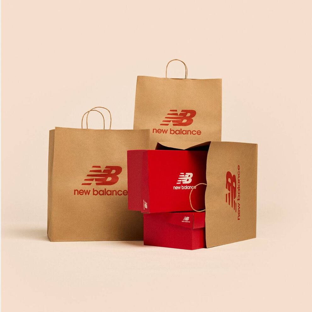 A group of New Balance branded bags and shoe boxes sitting on a beige background.