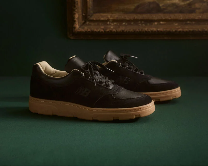 Knee down view of a man wearing a pair of New Balance Made in UK sneakers standing on a patterned tile floor.  