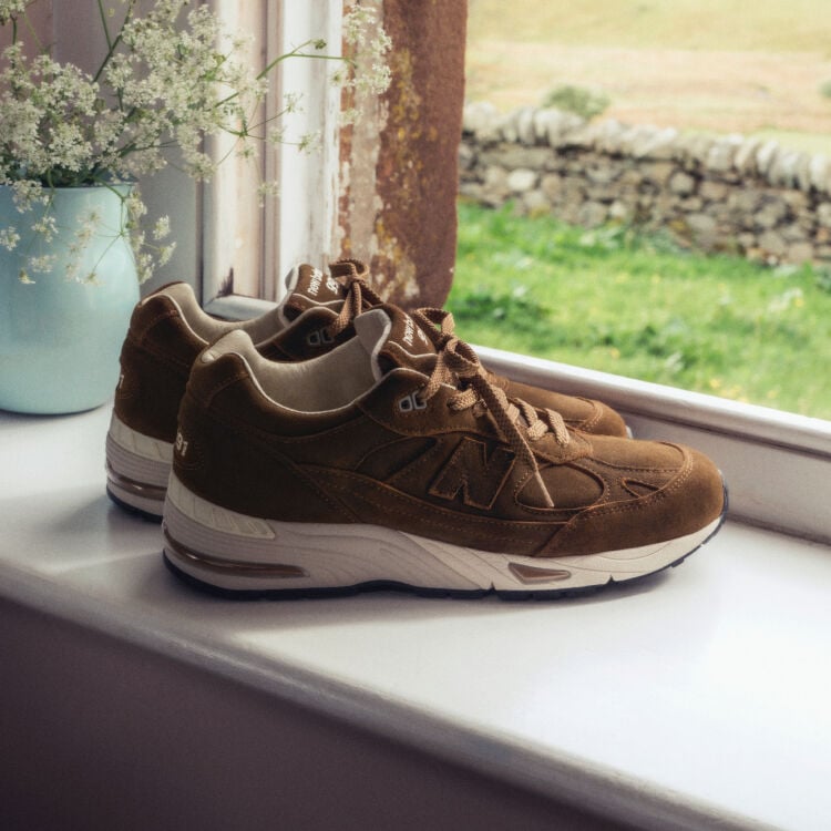 A pair of New Balance Made in UK sneakers on a windowsill next to a small vase of white flowers. 
