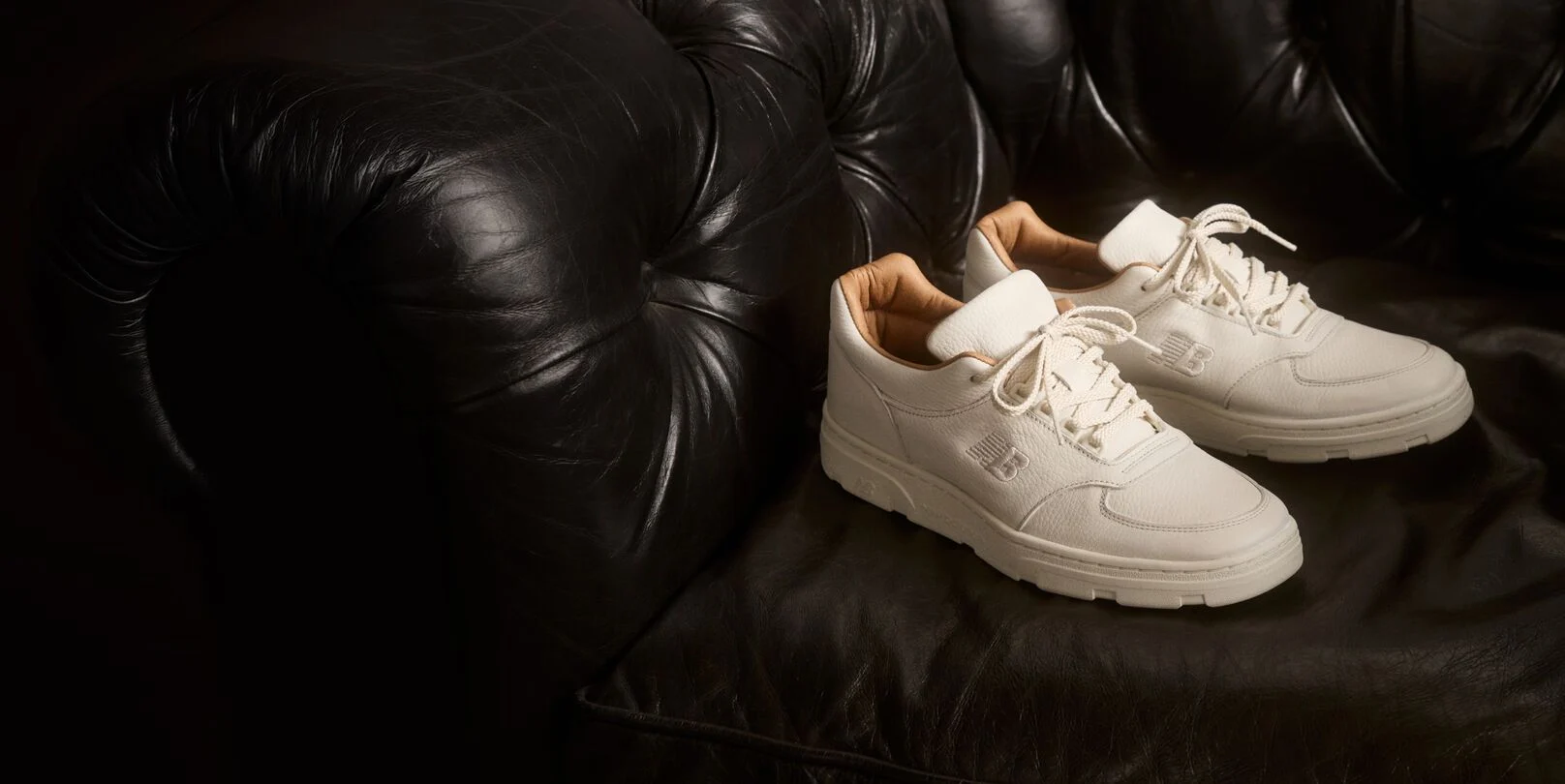 A pair of New Balance Made in UK sneakers sitting on a black leather sofa.