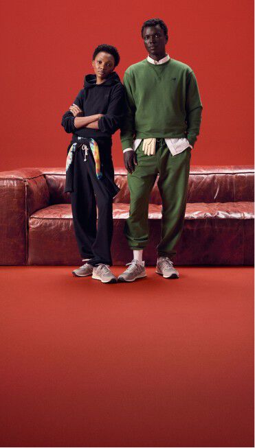 Couple wearing same color outfits standing on a red background in front of a red couch.