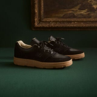 Knee down view of a man wearing a pair of New Balance Made in UK sneakers standing on a patterned tile floor.  