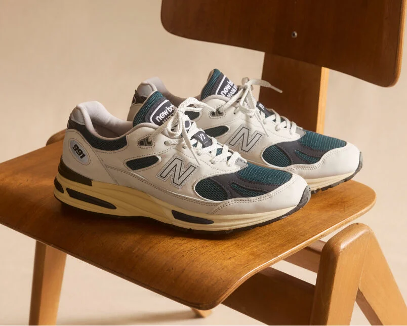 A pair of New Balance Made in UK sneakers in front of a rabbit in a brown textured studio environment. 