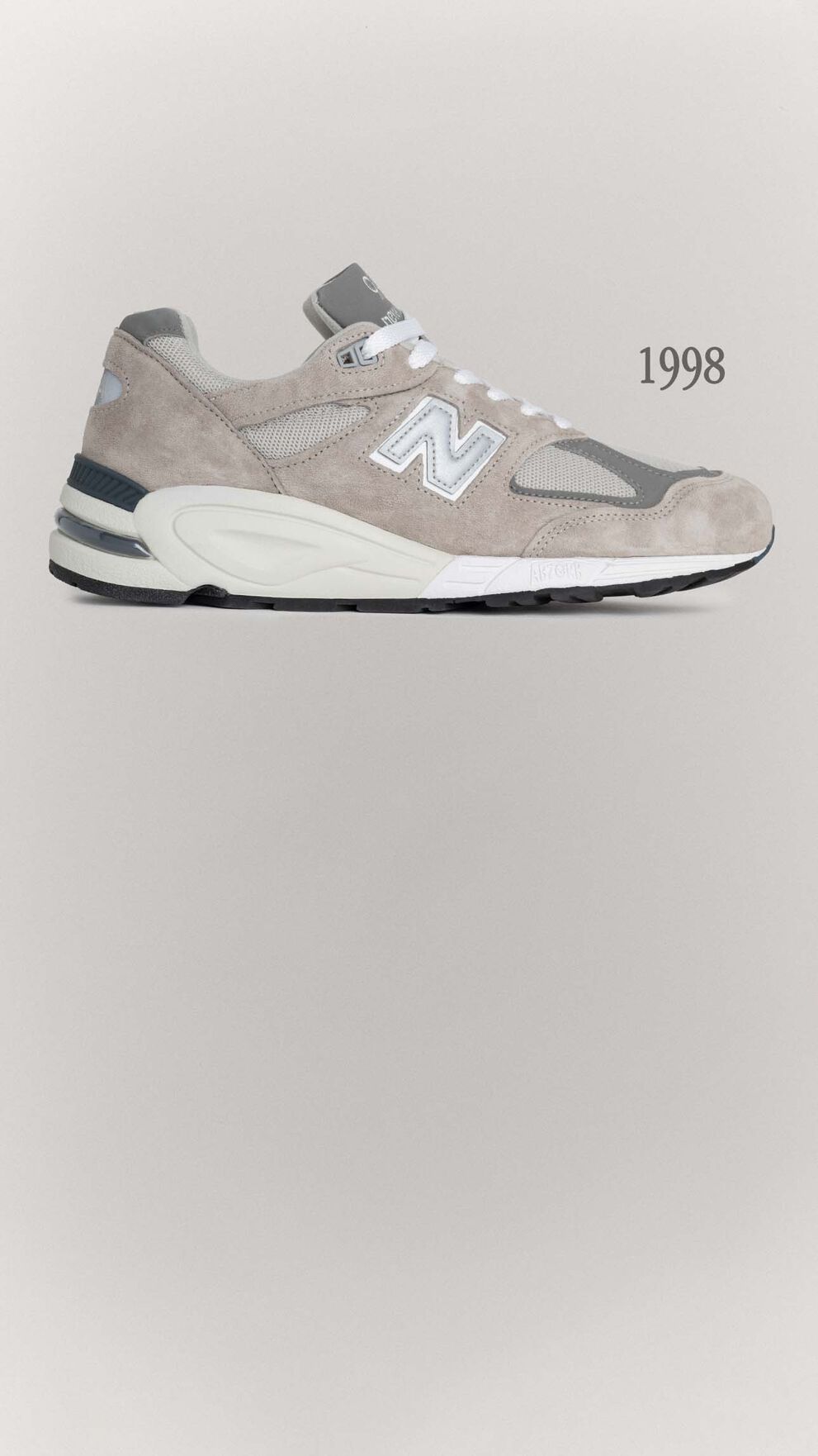 A grey 990v1 sneaker sitting on a grey background.