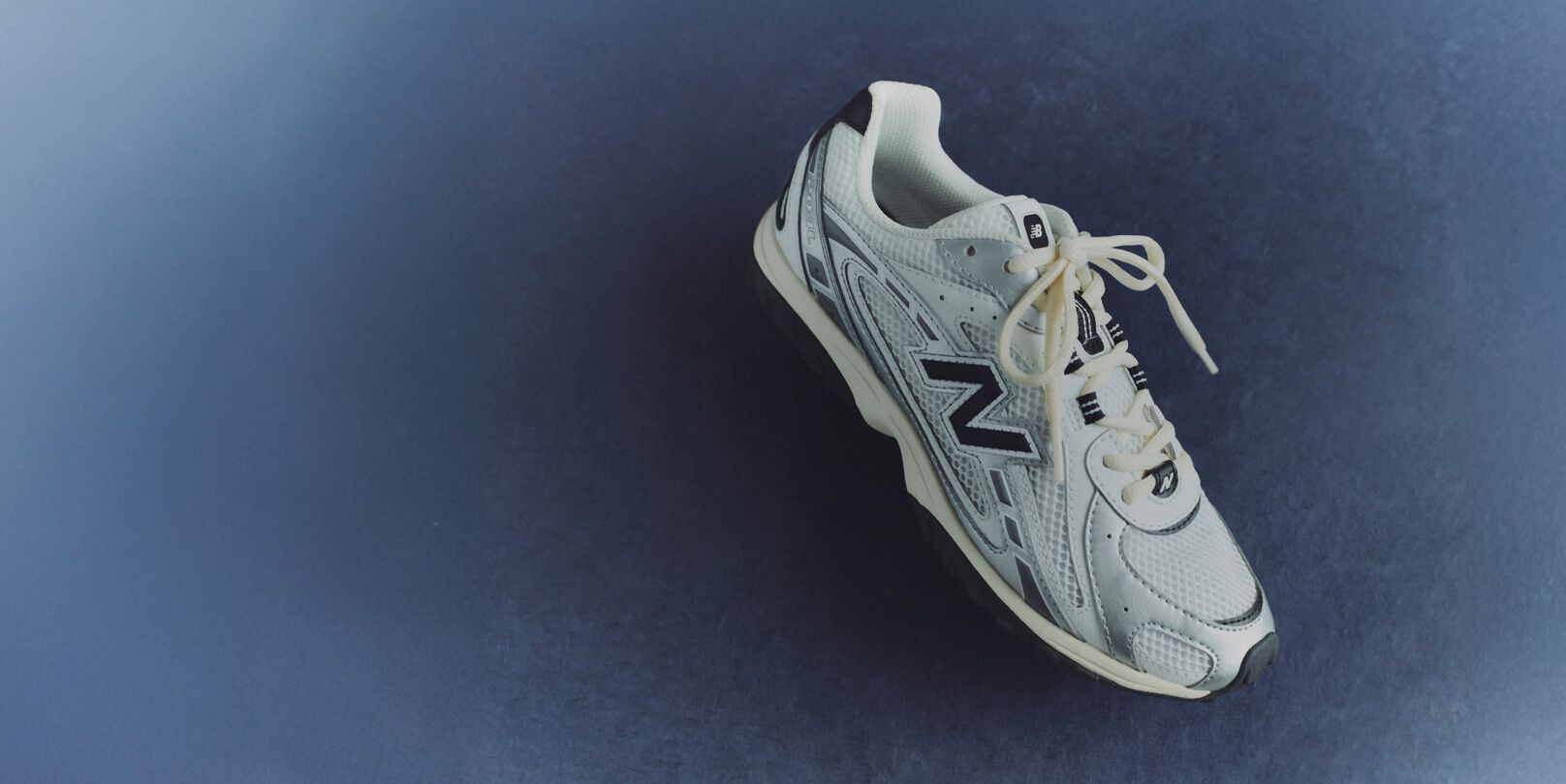 A pair of white and black 204L sneakers against a blue background.