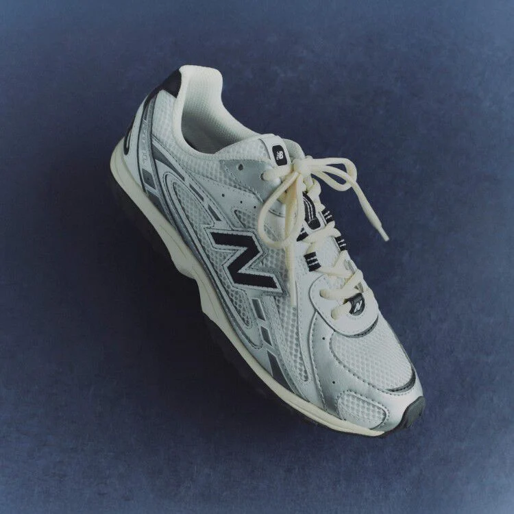 A pair of white and black 204L sneakers against a blue background.