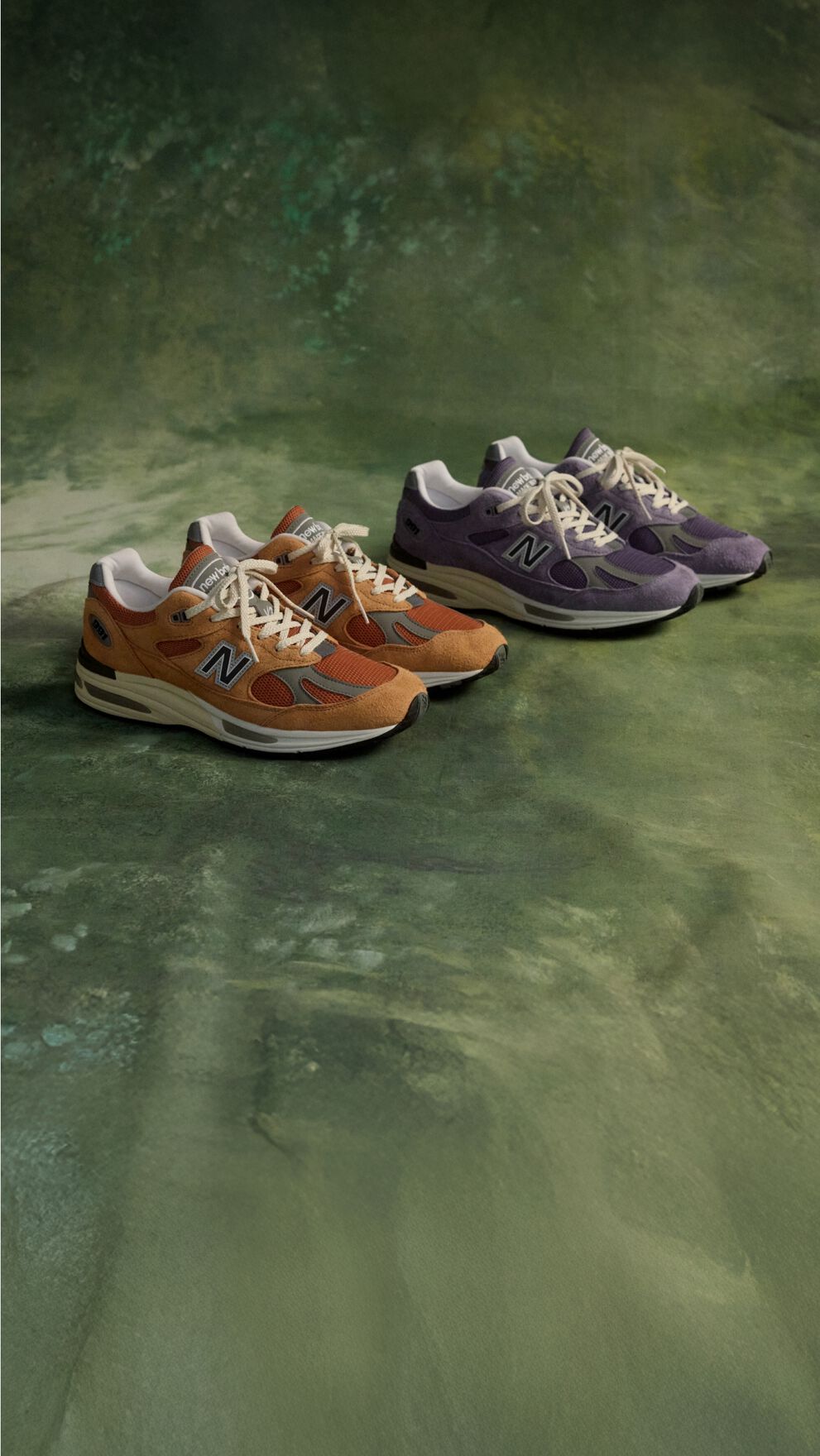 Two pairs of New Balance Made in UK sneakers on a green floor.