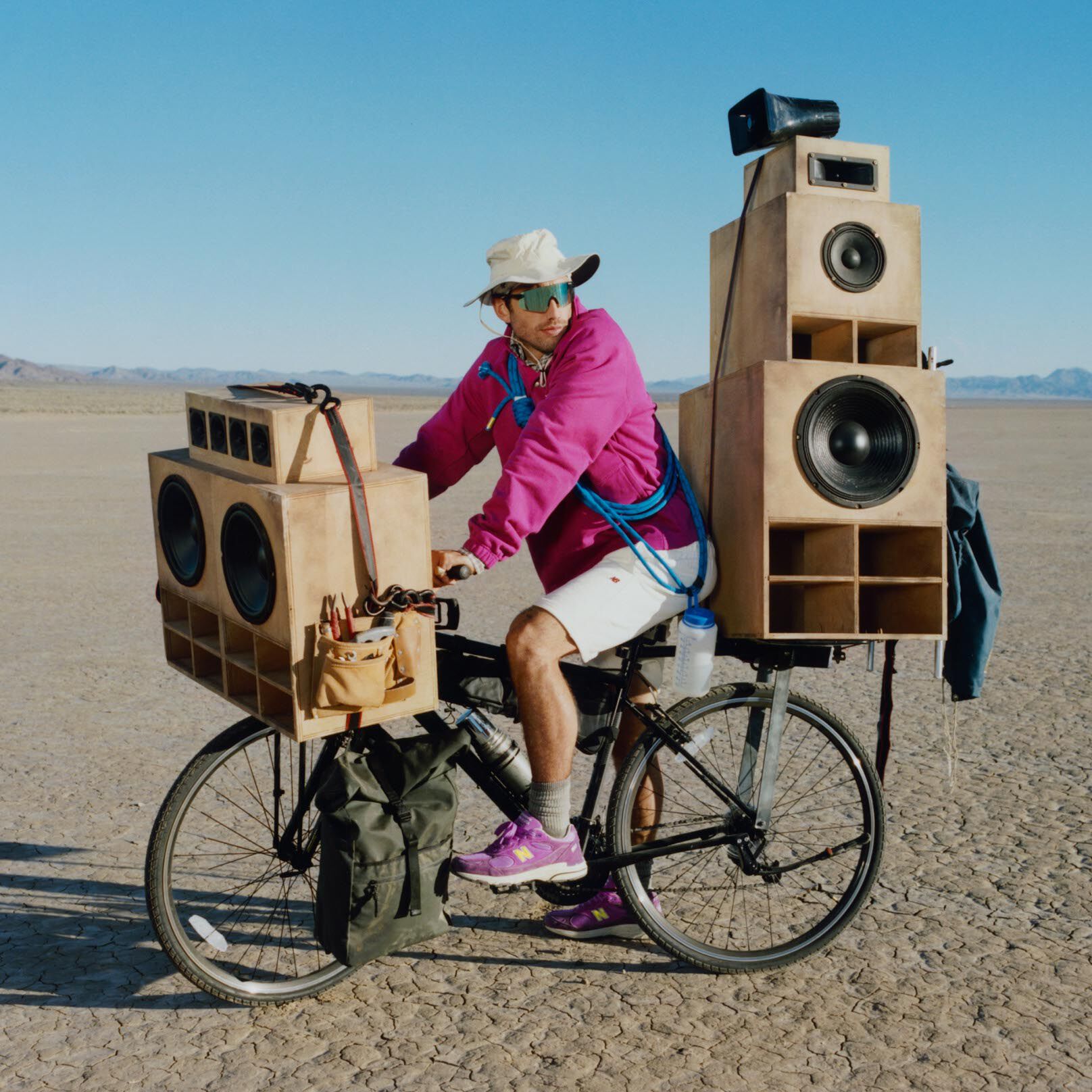 Guy on a bike with giant speakers attached to it wearing a New Balance purple sweater and shoes. 