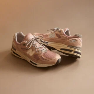 A pair of New Balance Made in UK sneakers in front of a rabbit in a brown textured studio environment. 