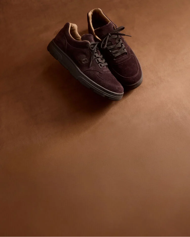 A pair of New Balance Made in UK sneakers in a brown textured studio environment. 