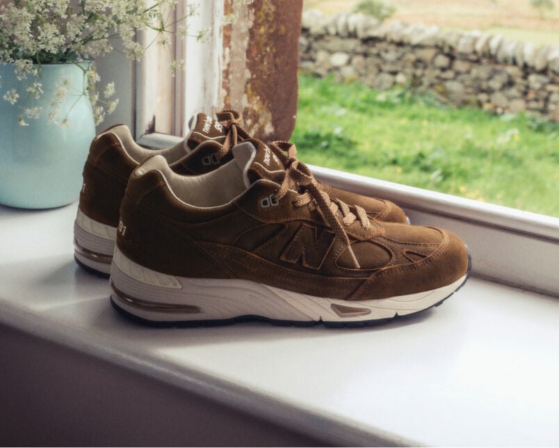 A pair of New Balance Made in UK sneakers sitting in a white studio environment. 