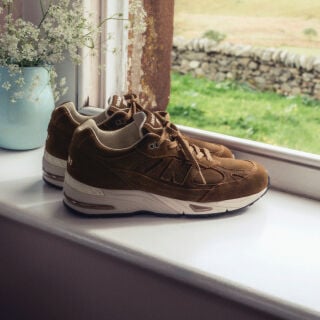A pair of New Balance Made in UK sneakers sitting in a white studio environment. 