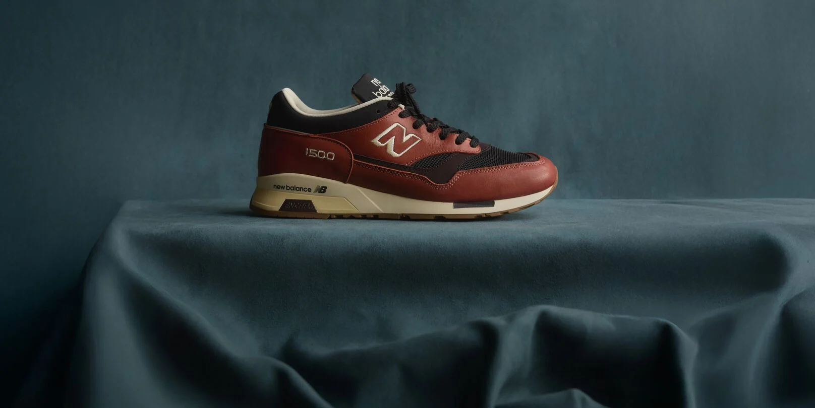 A New Balance Made in UK sneaker sitting in a flowing blue fabric studio backdrop. 